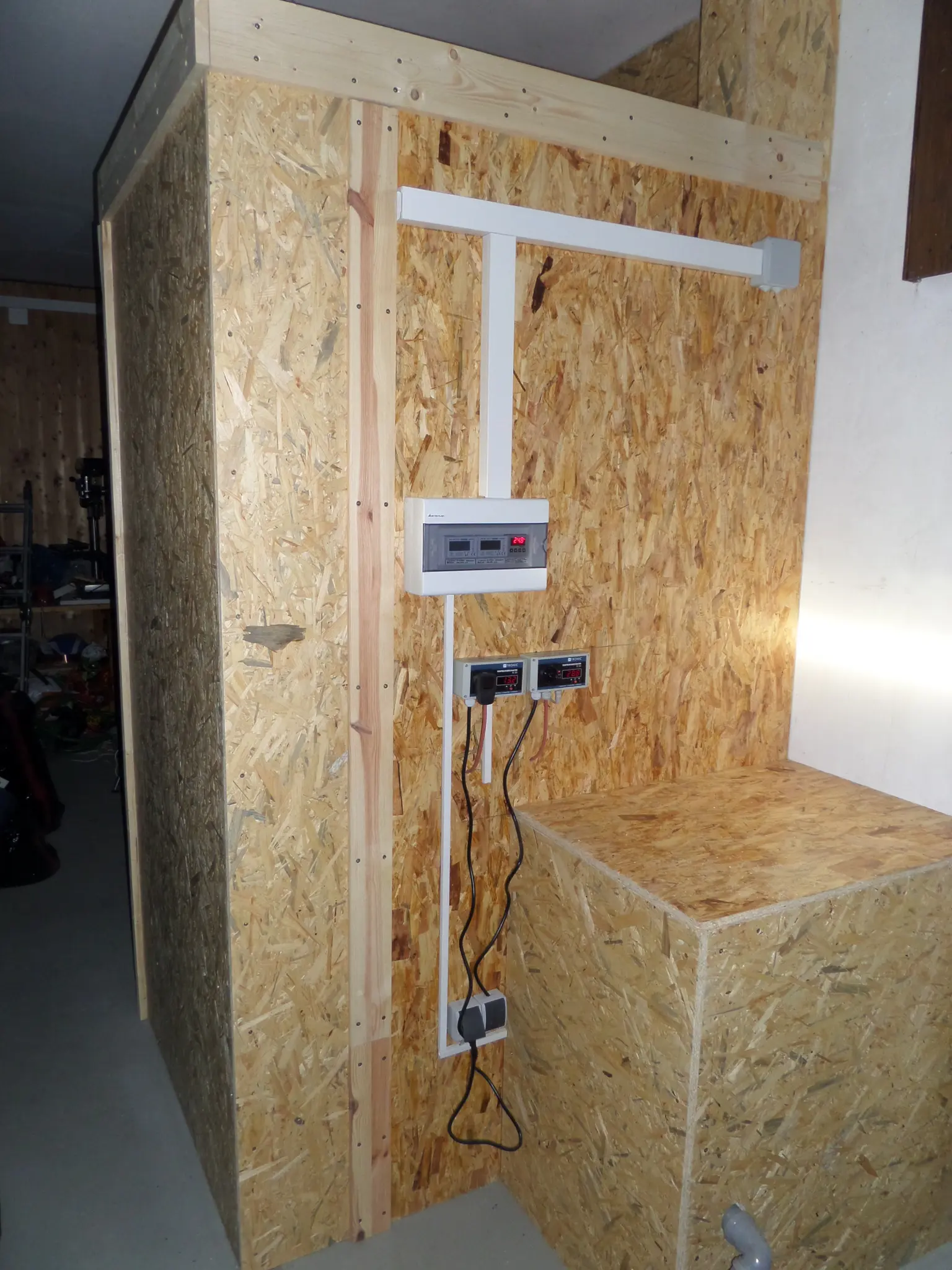 Wooden structure with a mounted electronic control panel and cables in a workshop or garage setting.