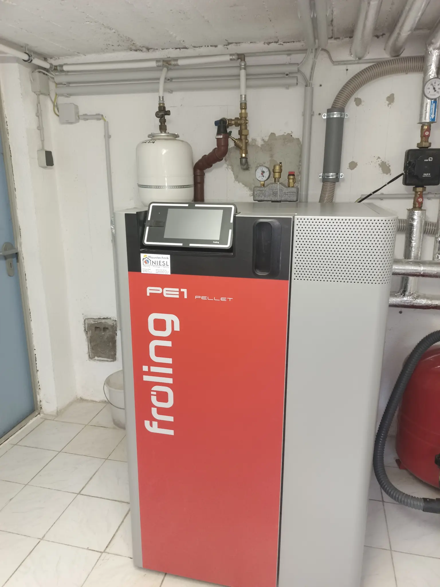 Two large gray cylindrical water heaters in tiled basement room with visible pipes and gauges.