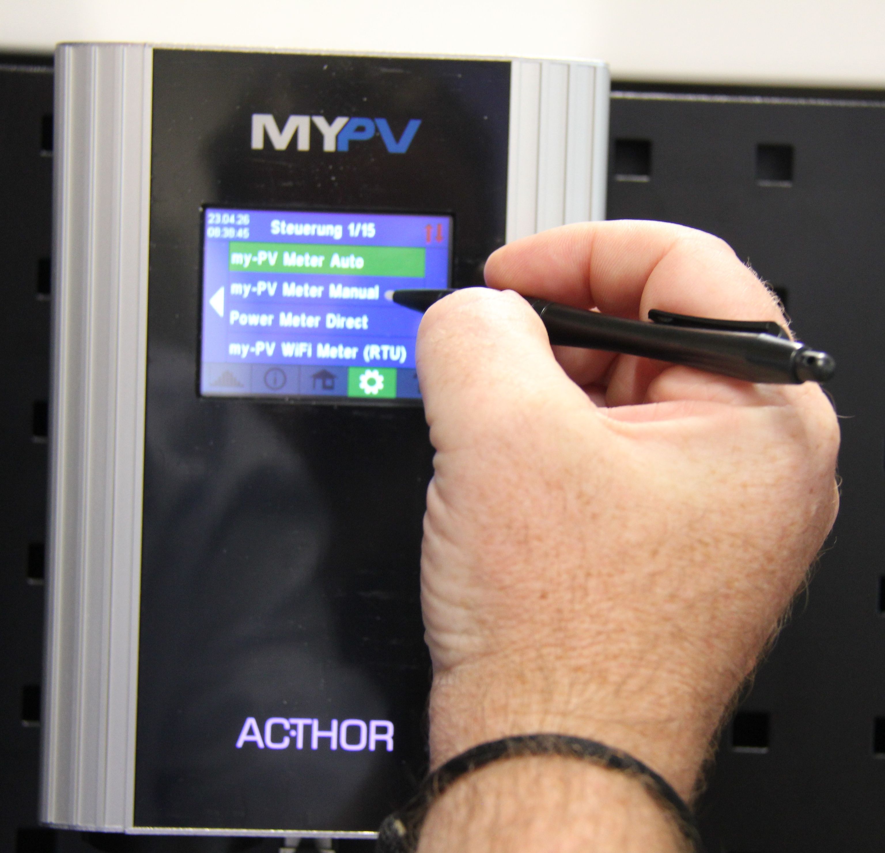 Hand using a stylus to operate a MYPV device with a digital screen displaying various settings like "my-PV Meter Manual."