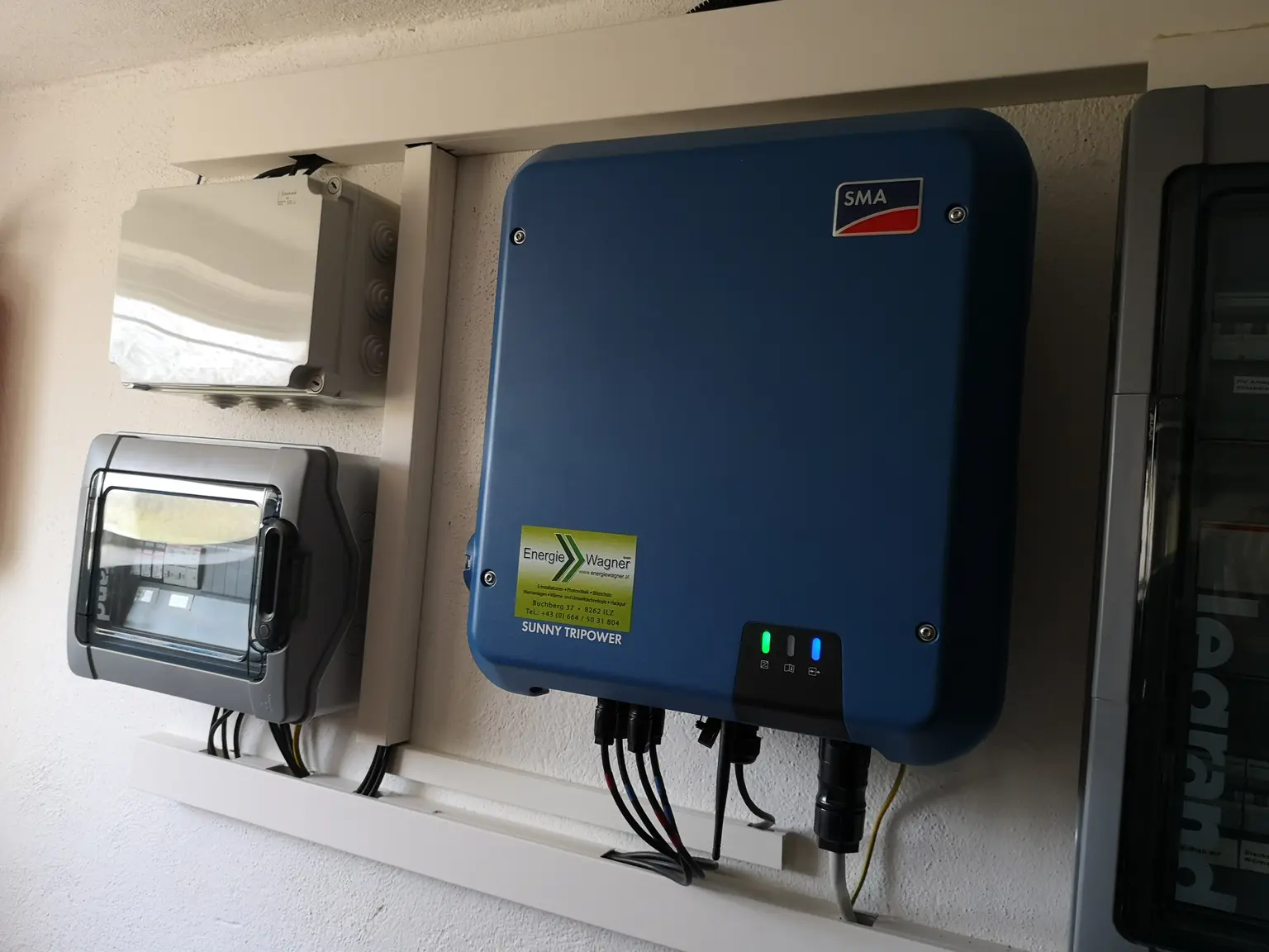 Blue SMA solar inverter mounted on a wall, connected to electrical boxes, in a clean, organized setup.
