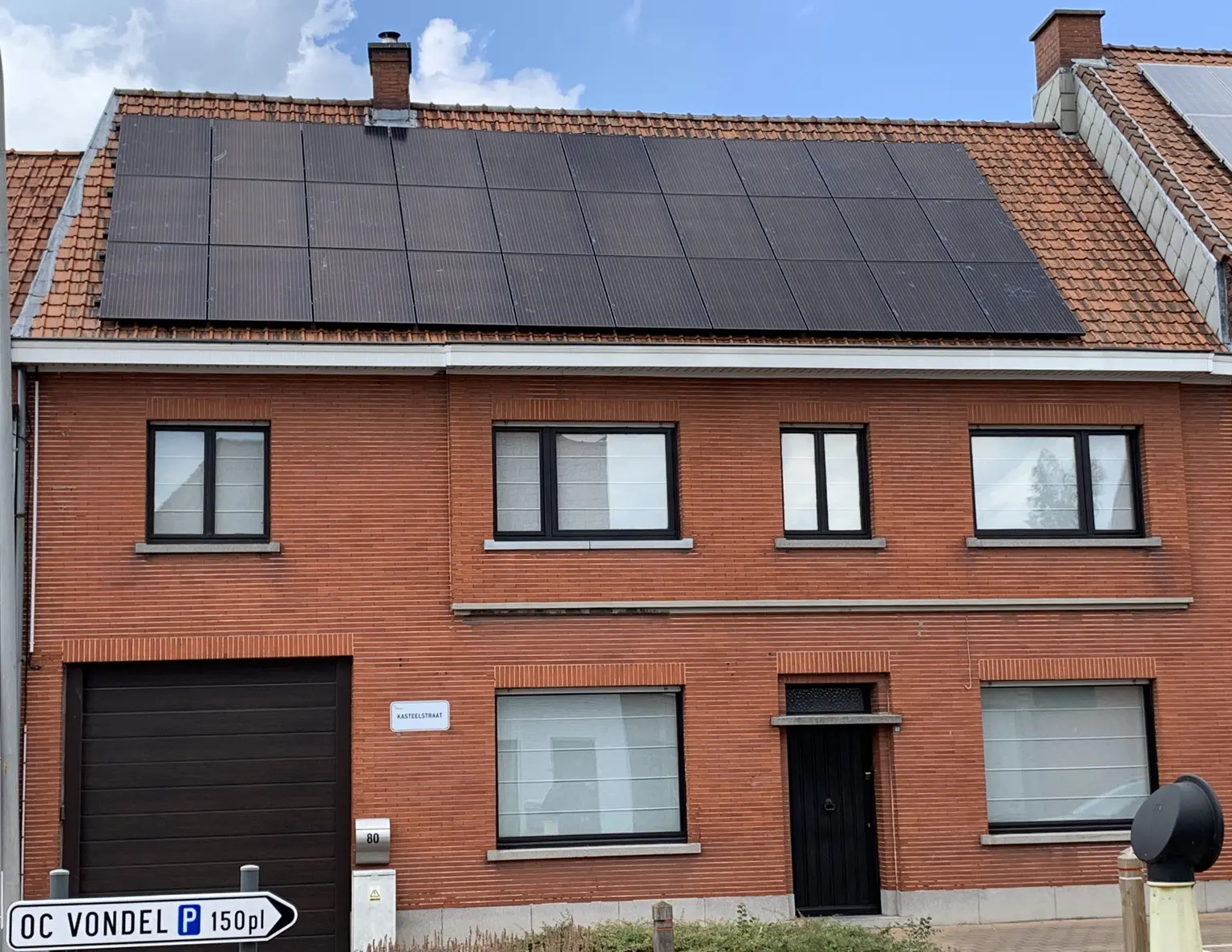 House with red brick facade featuring dark brown windows and door with photovoltaic panels on the roof