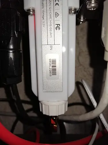 Close-up of a white electronic device with a barcode and serial number, surrounded by red and black cables.