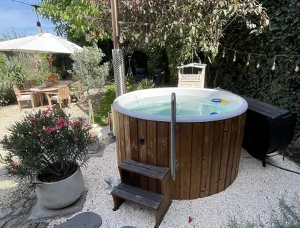 Jacuzzi with wooden cladding and a rubber duck inside, fairy lights above and greenery all around