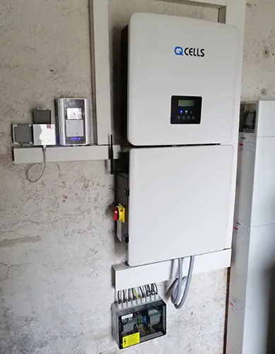 Wall-mounted Q CELLS solar inverter system with my-PV AC•THOR, control panel, and cables, installed on a textured wall.