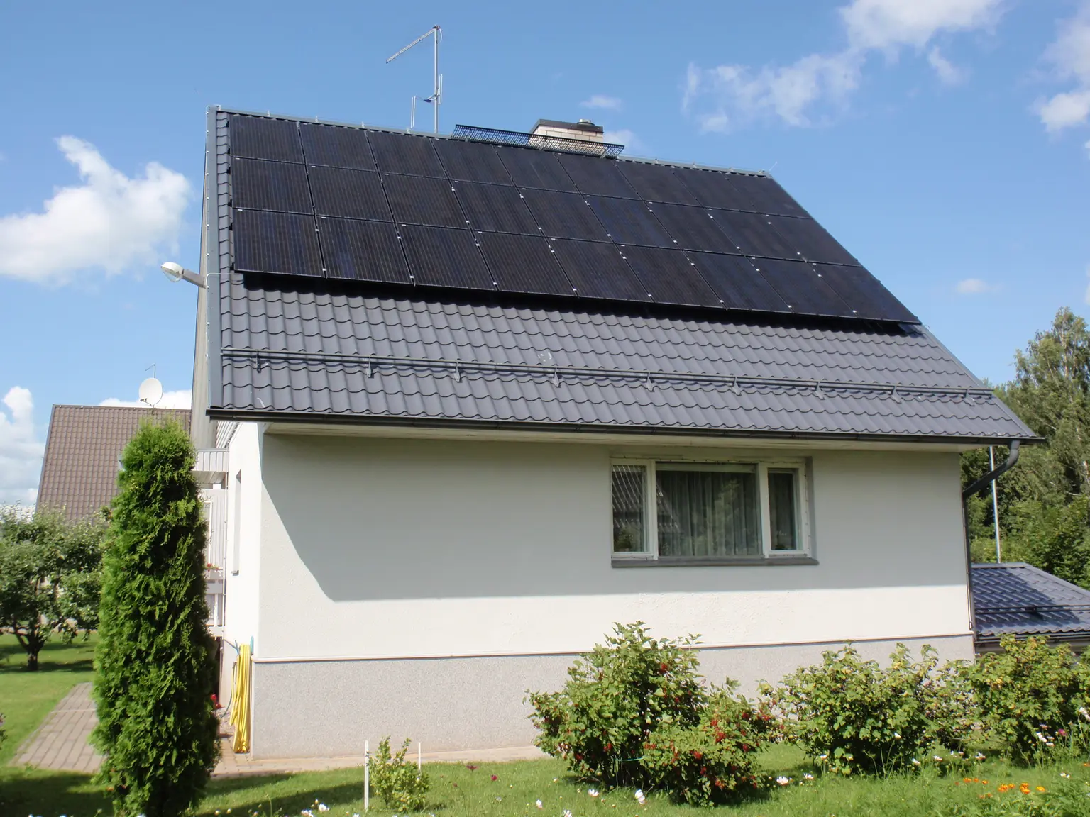 Rear view of a house with PV panels on the roof and various bushes in the garden foreground.