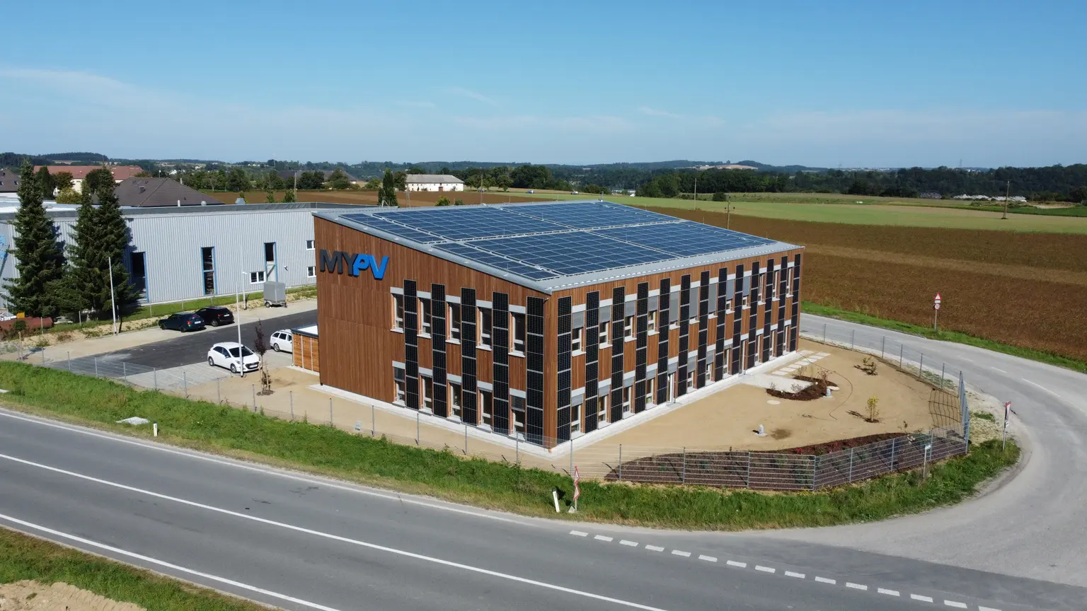 Company building viewed from above at an angle, with PV panels on roof and facade. Garden is newly landscaped around.