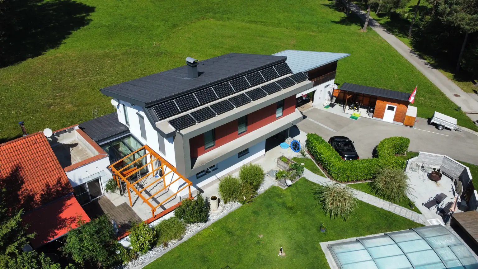 Solar panels on roof of modern architect’s house with large driveway, big garden, pool, and dog looking up from garden.