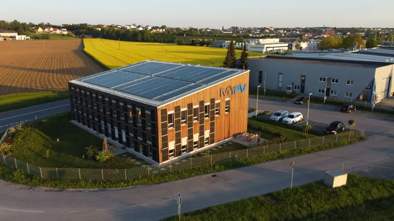 Aerial view of my-PV building with solar panels on roof and facade, visible logo, and cars in the parking lot.