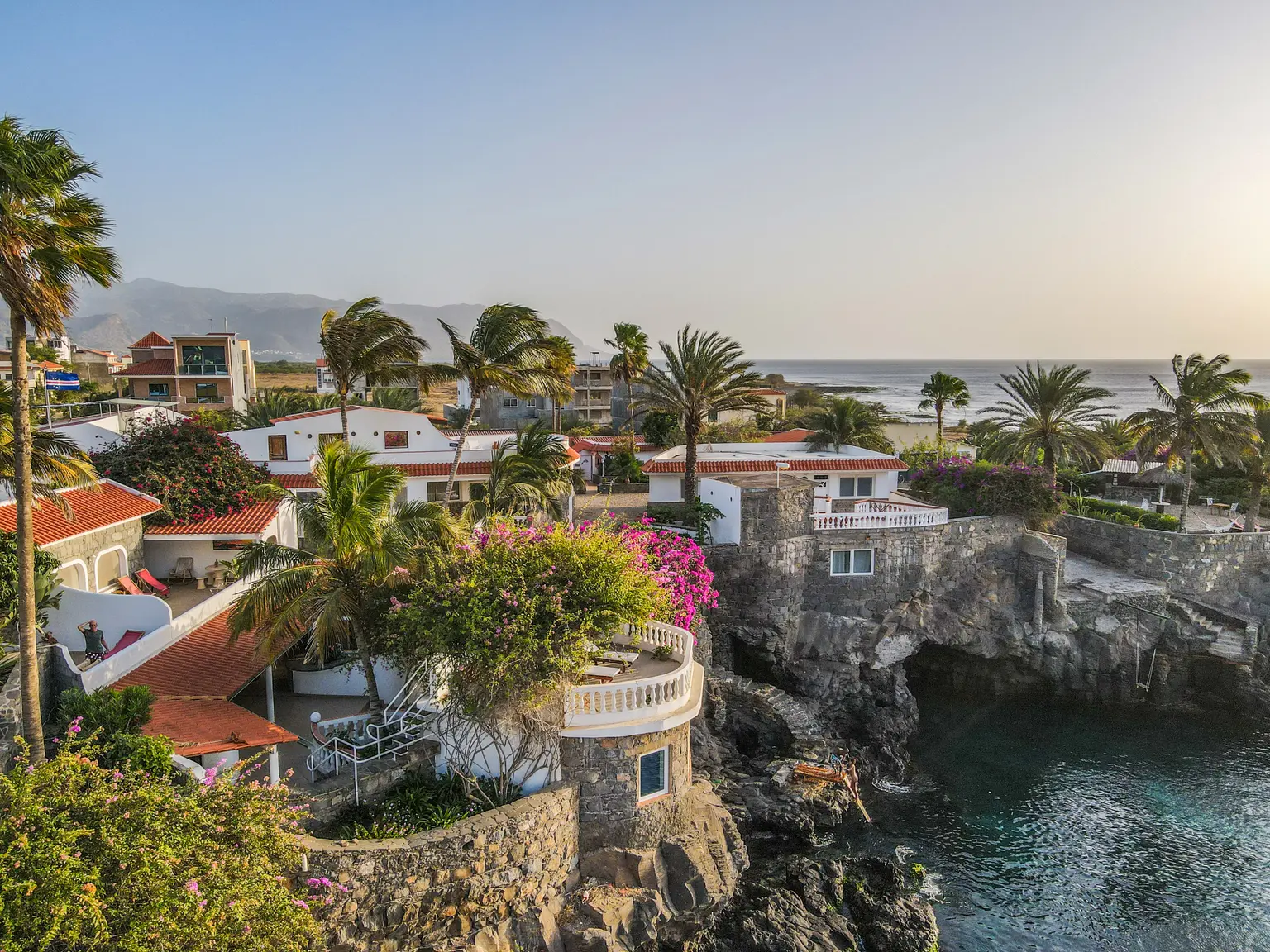 Hotel complex on sea cliffs with balconies, pool, palms and surrounding shrubs