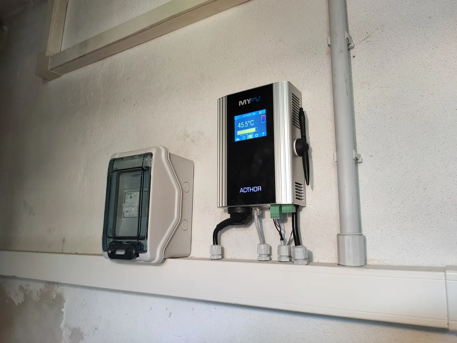 Wall-mounted electrical device with digital display showing '45°C' and a protective cover beside it on a white wall.