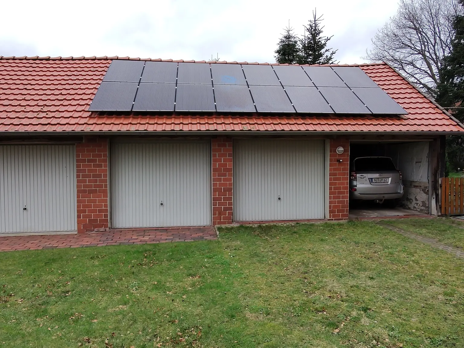 Garage with red brick wall, four garage doors, and photovoltaic panels installed on the roof.
