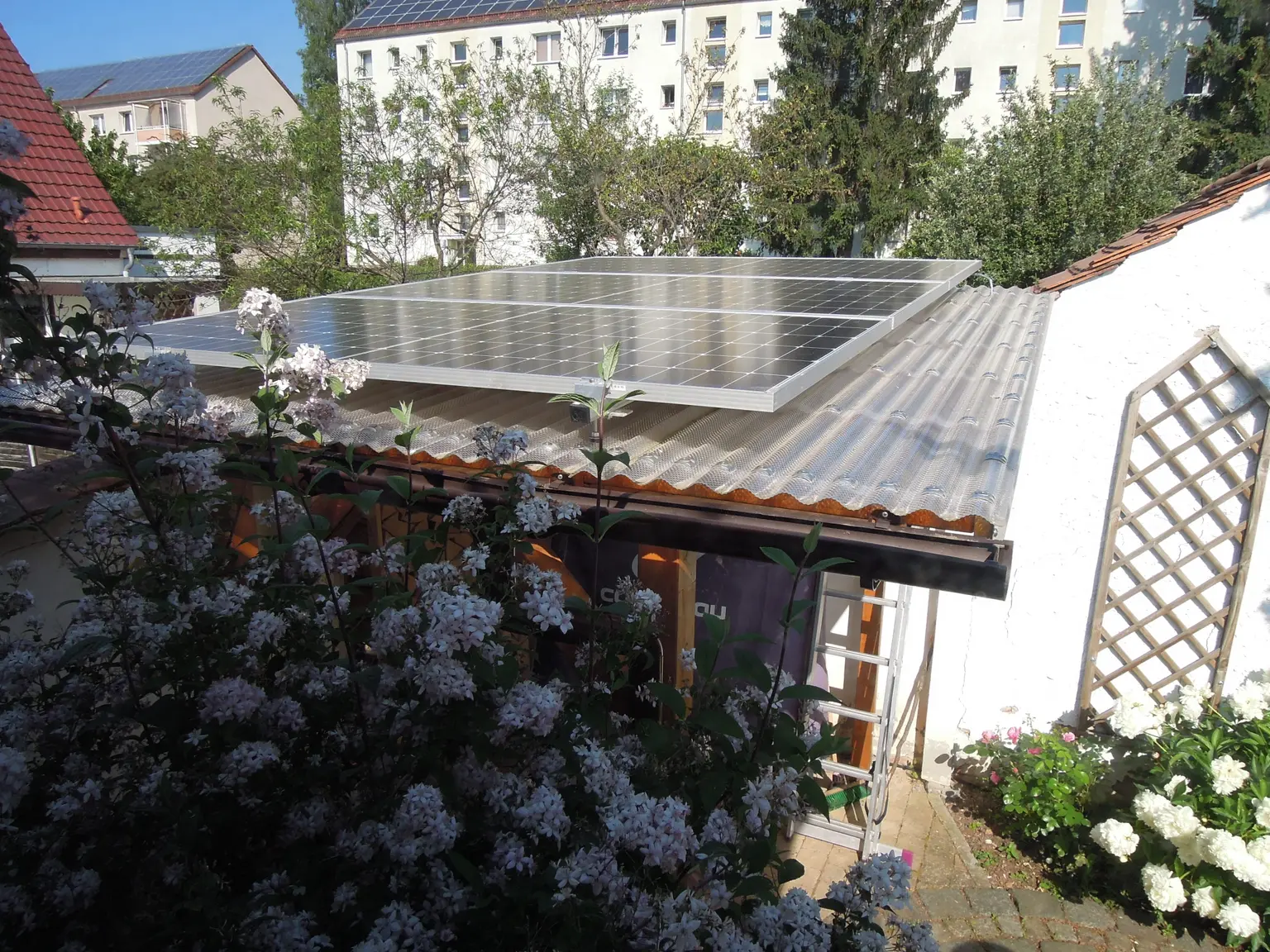 PV panels with 1.4 kWp on a small garden shed roof, with a large flowering plant in front.