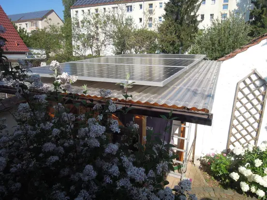PV panels with 1.4 kWp on a small garden shed roof, with a large flowering plant in front.
