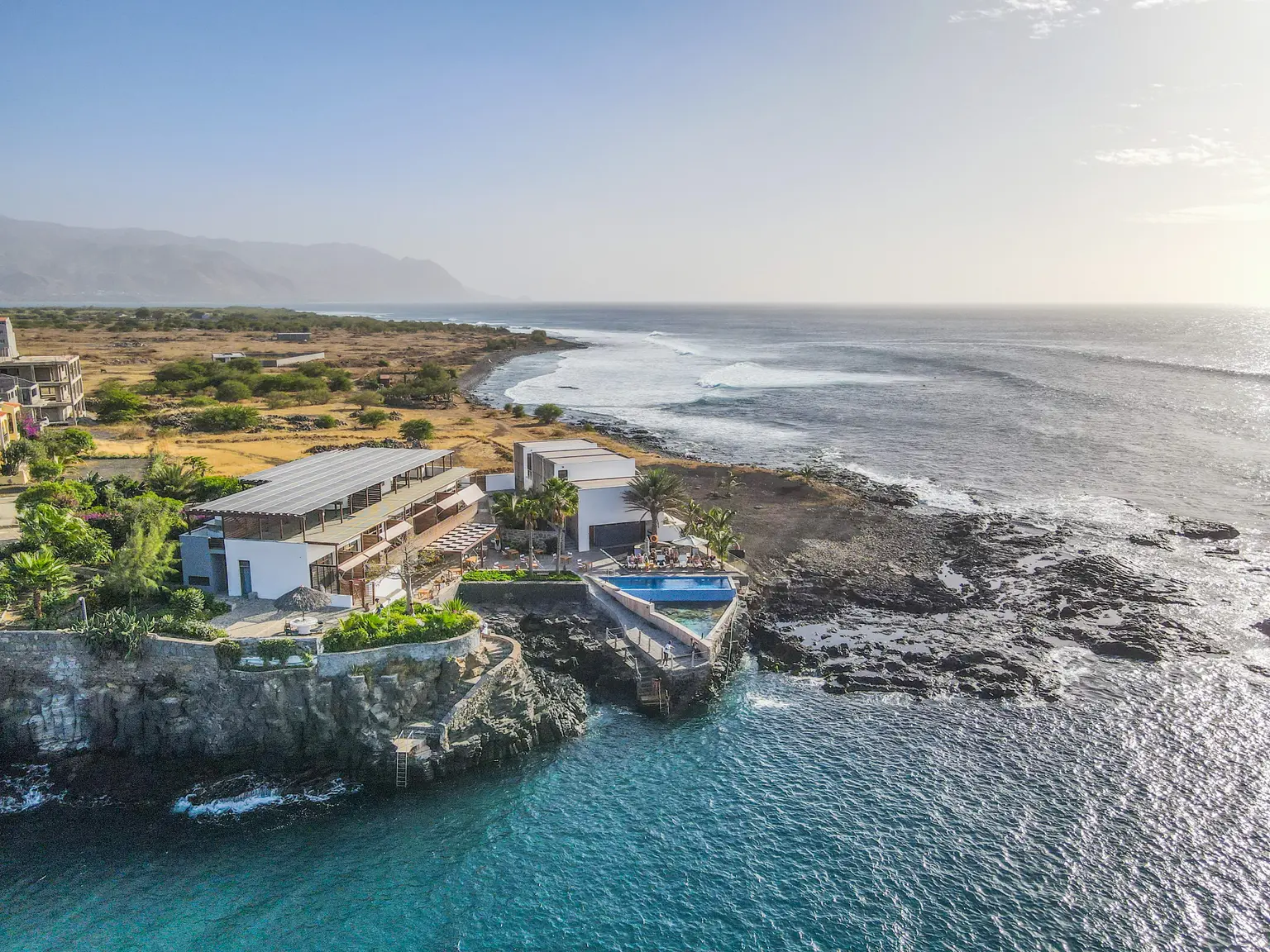 Hotel complex on sea cliffs with pool, palms and shrubs