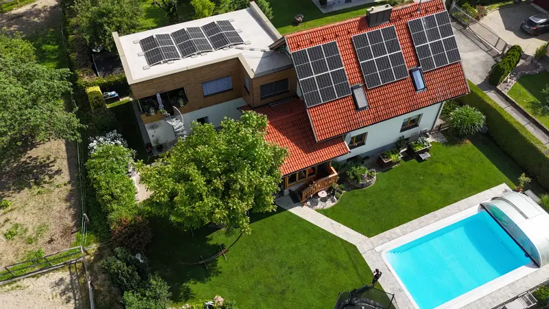 Aerial view of a renovated family home with rooftop PV system, landscaped garden, and swimming pool.