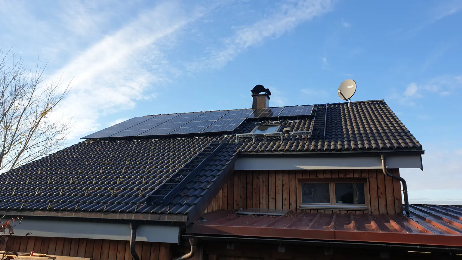 House with roof facade featuring a chimney, satellite dish, and PV panels.