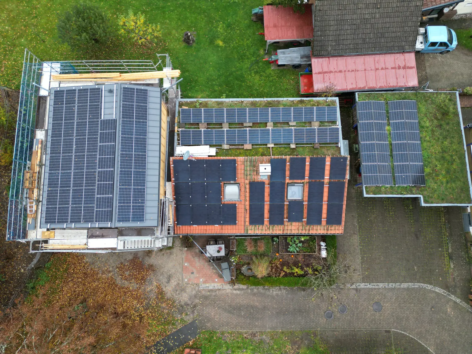 Single-family house with extensions, full solar-panel roof, green garden, viewed in an autumn setting.