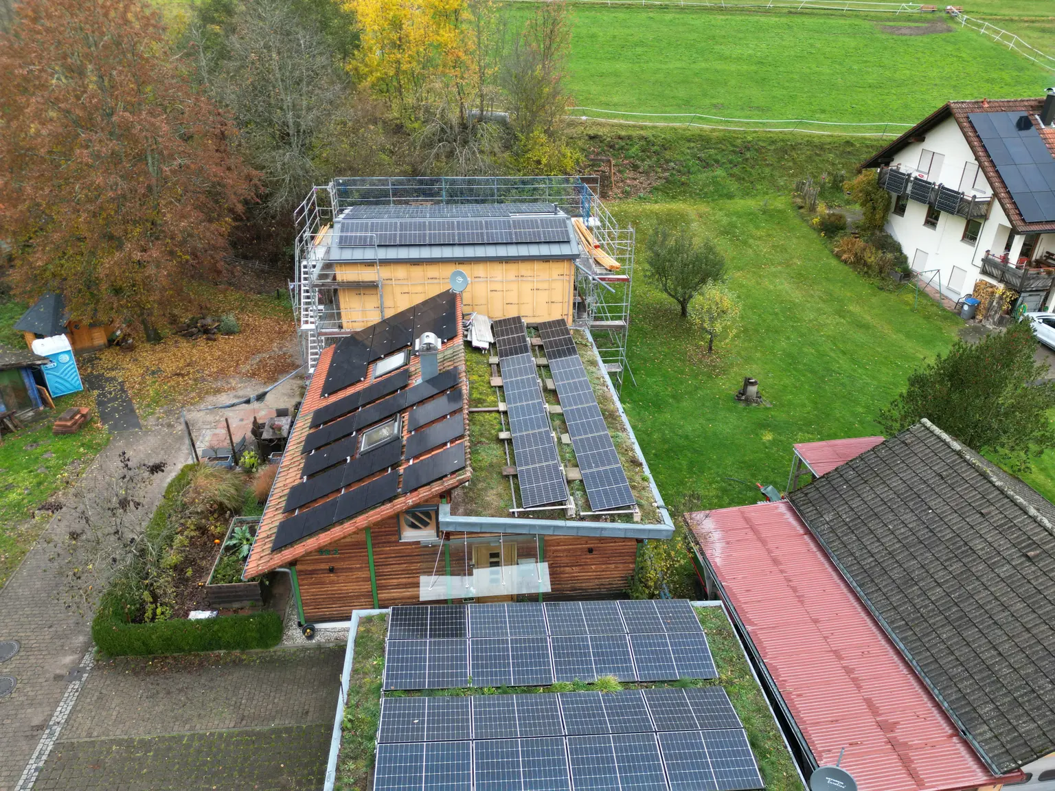 Angled top view of house with half-green, half-tiled roof, solar panels, wooden facade, and an extension with panels.