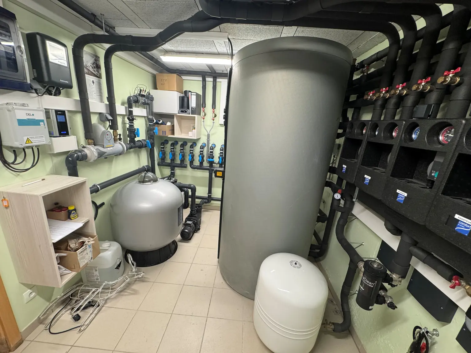 Utility room with large cylindrical tanks, pipes, and wall-mounted control panels for managing building or water systems