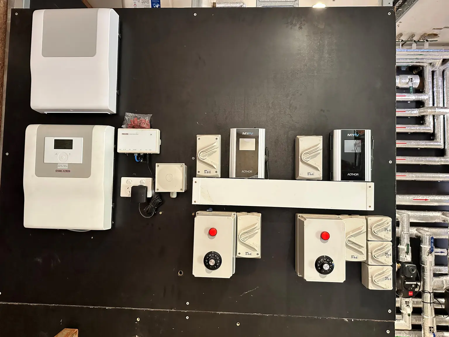 Black panel with electrical devices, including switches, controllers, and power unit, neatly arranged and mounted.