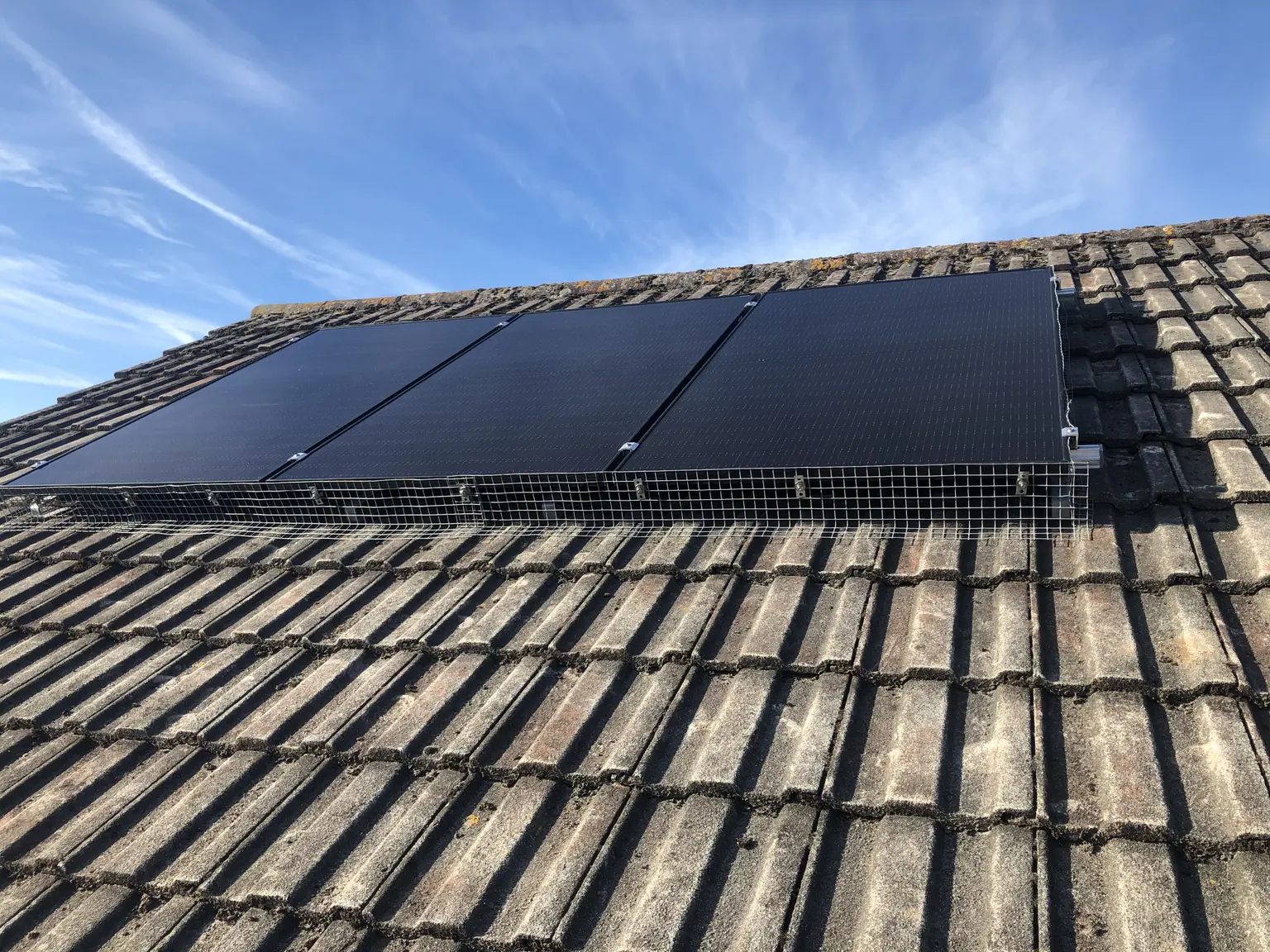 PV panels on the roof under a blue sky with a few clouds drifting across in the background