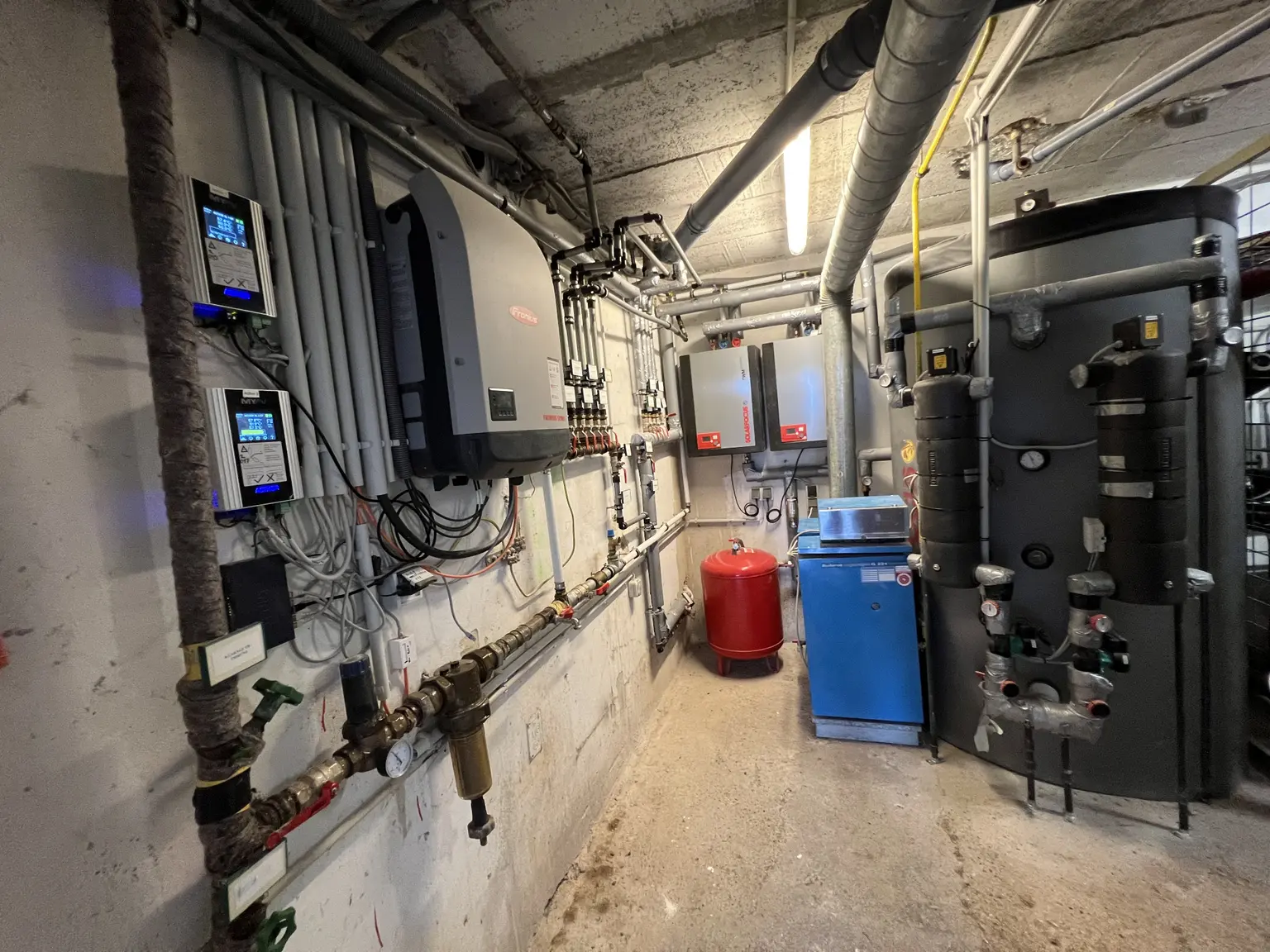 Basement room with water heater, many pipes, a Fronius inverter, and two AC Thor 9s units.