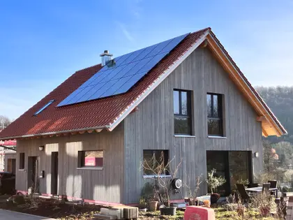 Modern single-family house with wood facade and PV panels on the roof, autumn setting and patio furniture on the terrace.