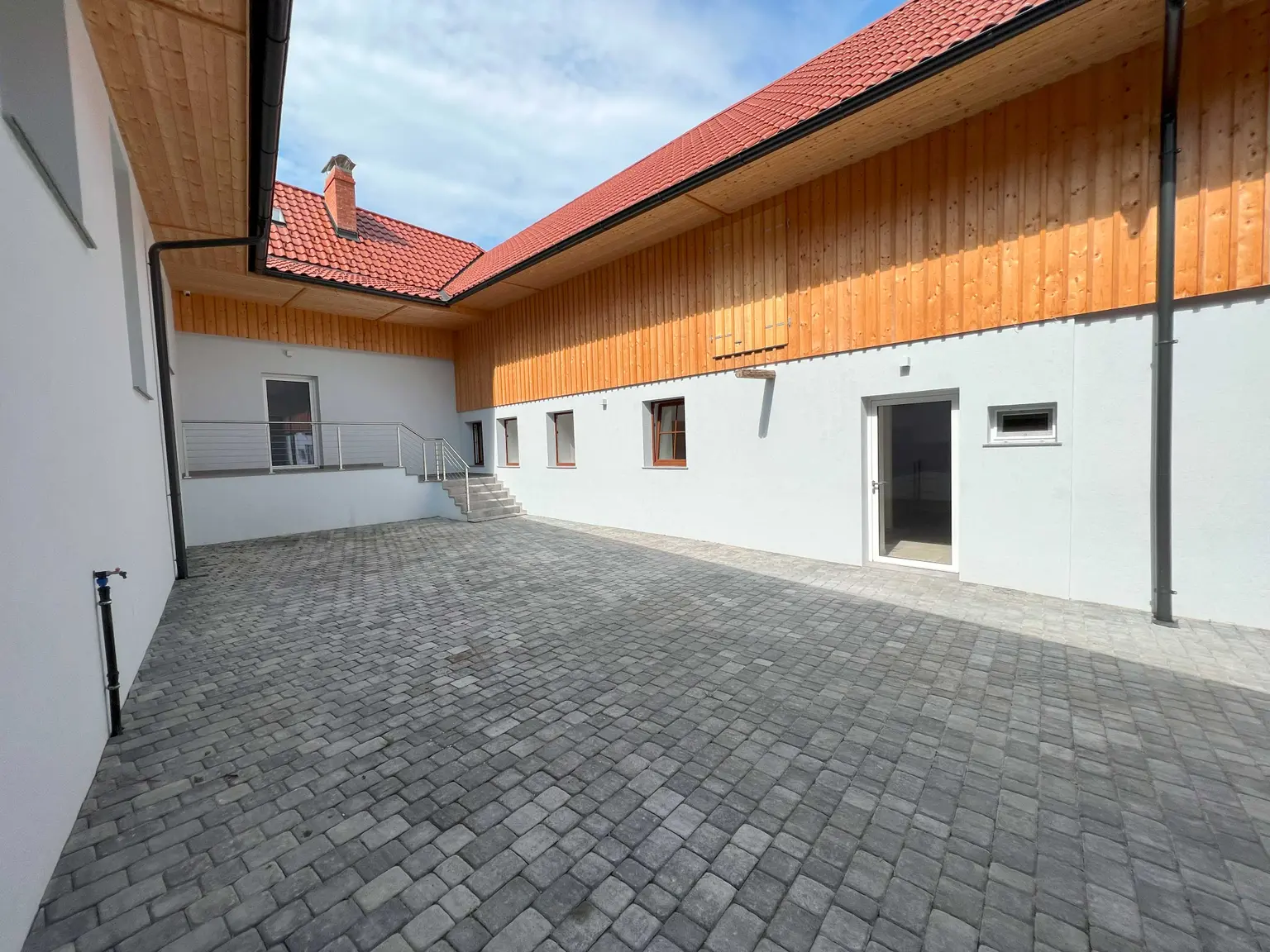 Small farmhouse courtyard with stone floor, white lower facade, and wooden upper facade.