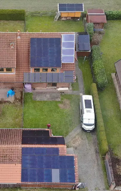 Aerial view of semi-detached houses with solar panels on roofs, green lawn, and a white van parked in the driveway