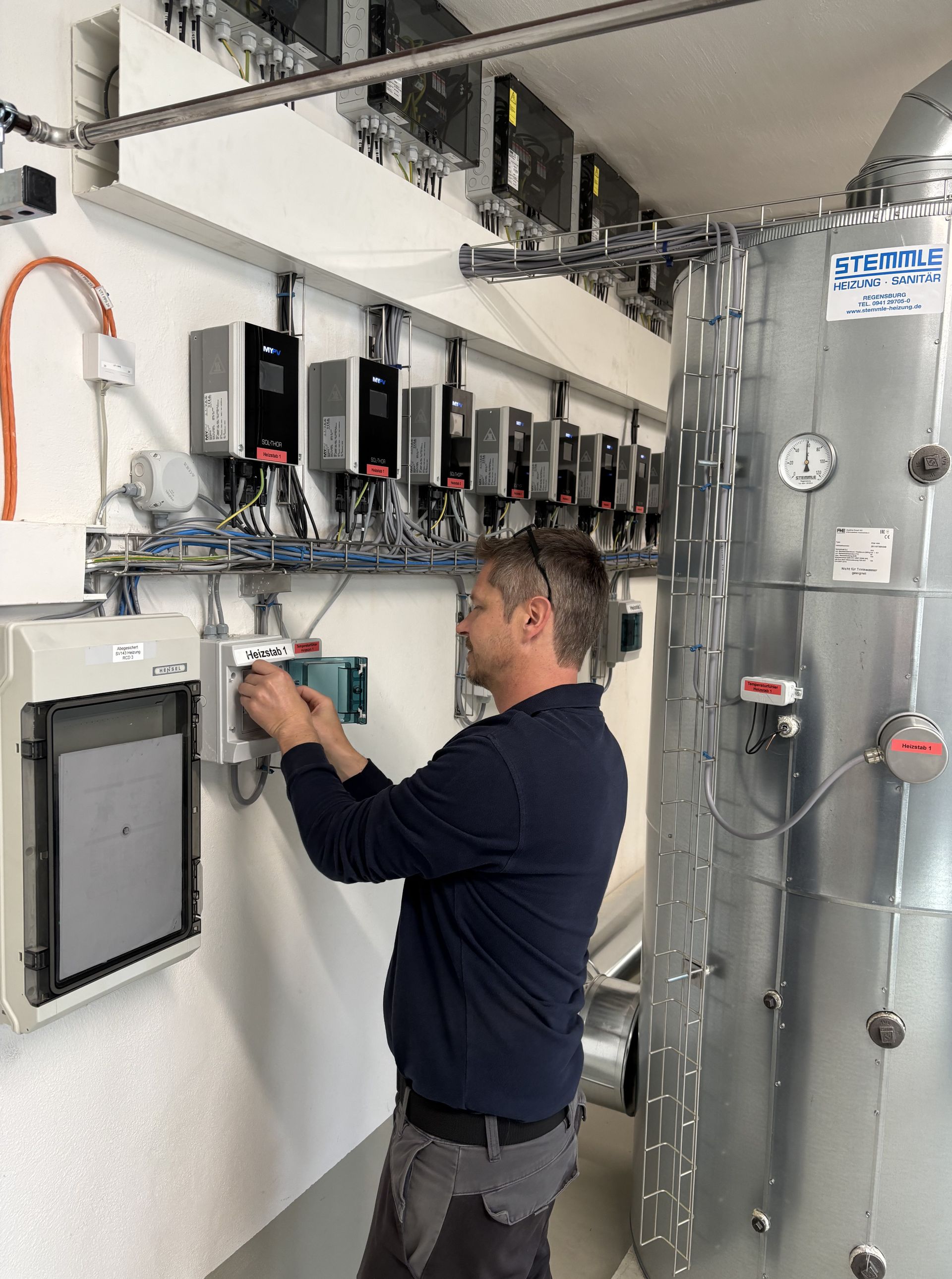 SOL•THOR units and commissioning, A person adjusting electrical equipment on a control panel in a utility room with multiple devices and cables mounted on the wall.