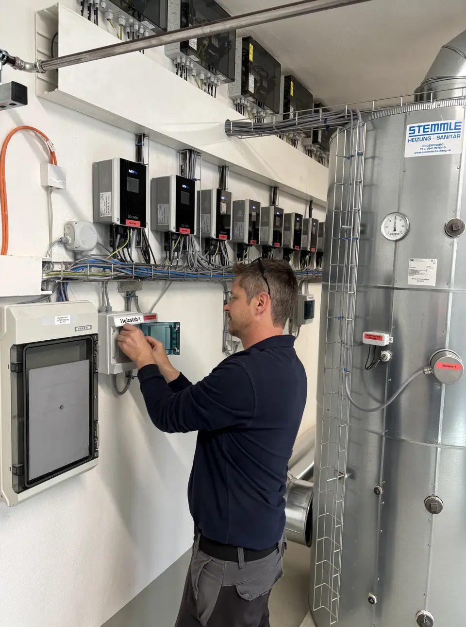 SOL•THOR units and commissioning, A person adjusting electrical equipment on a control panel in a utility room with multiple devices and cables mounted on the wall.