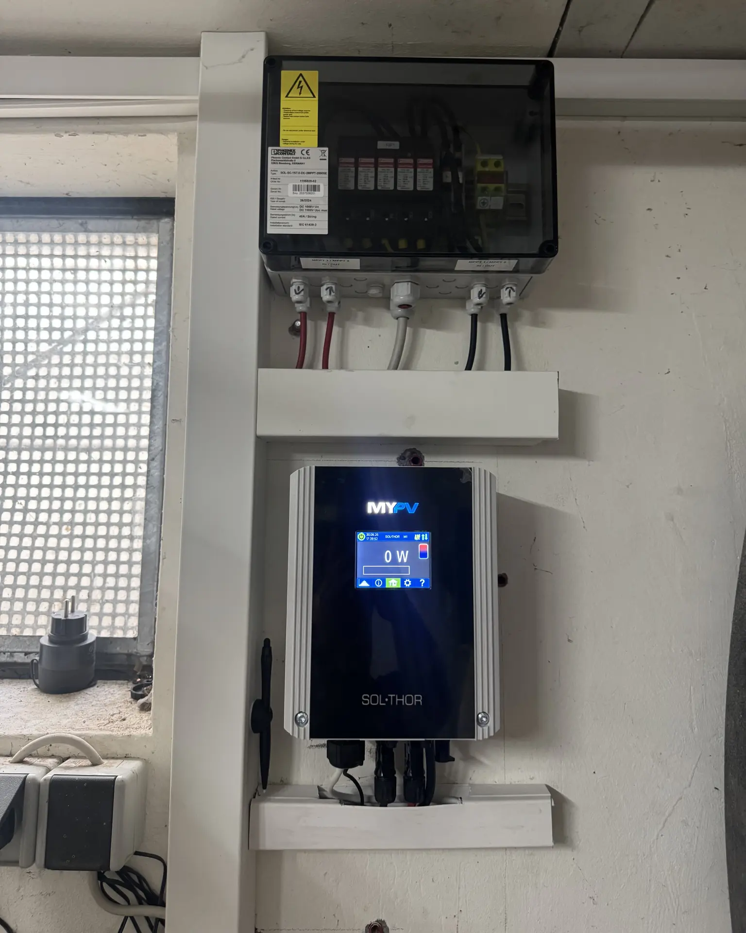 A wall-mounted electrical setup with a black-boxed circuit breaker above a digital display unit labeled "MY PV SO-THOR."