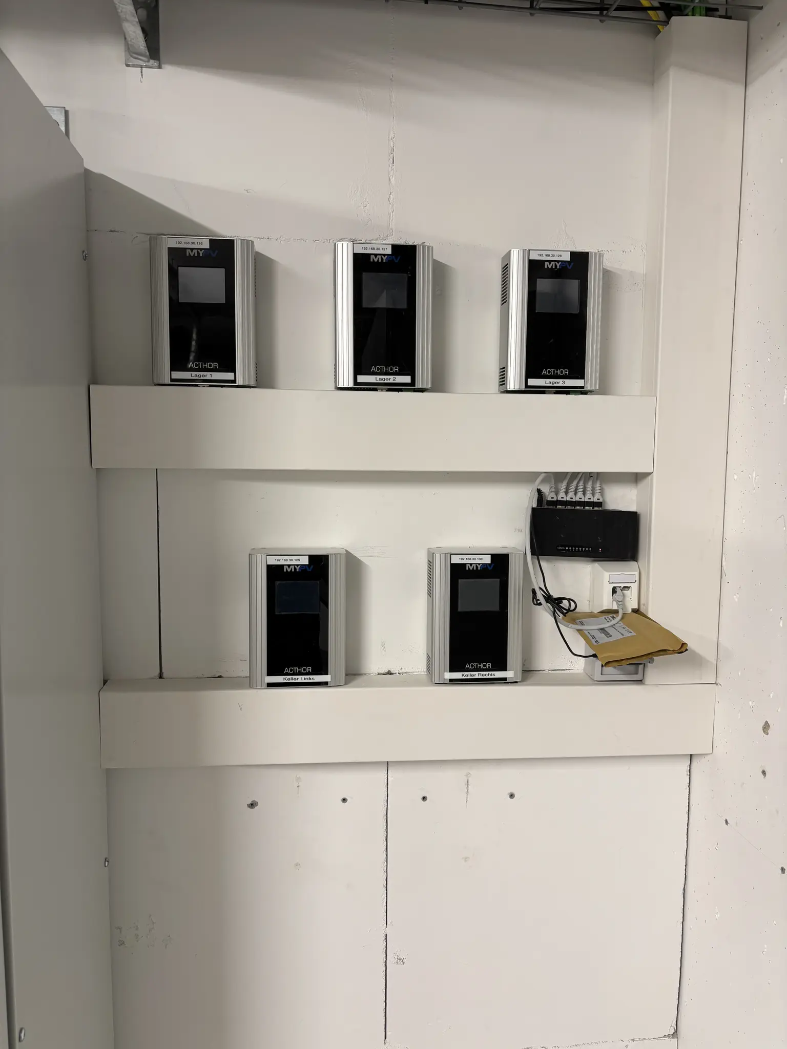 Five wall-mounted MYPV Acthor devices on white shelves, with connected network equipment and wiring on the right.