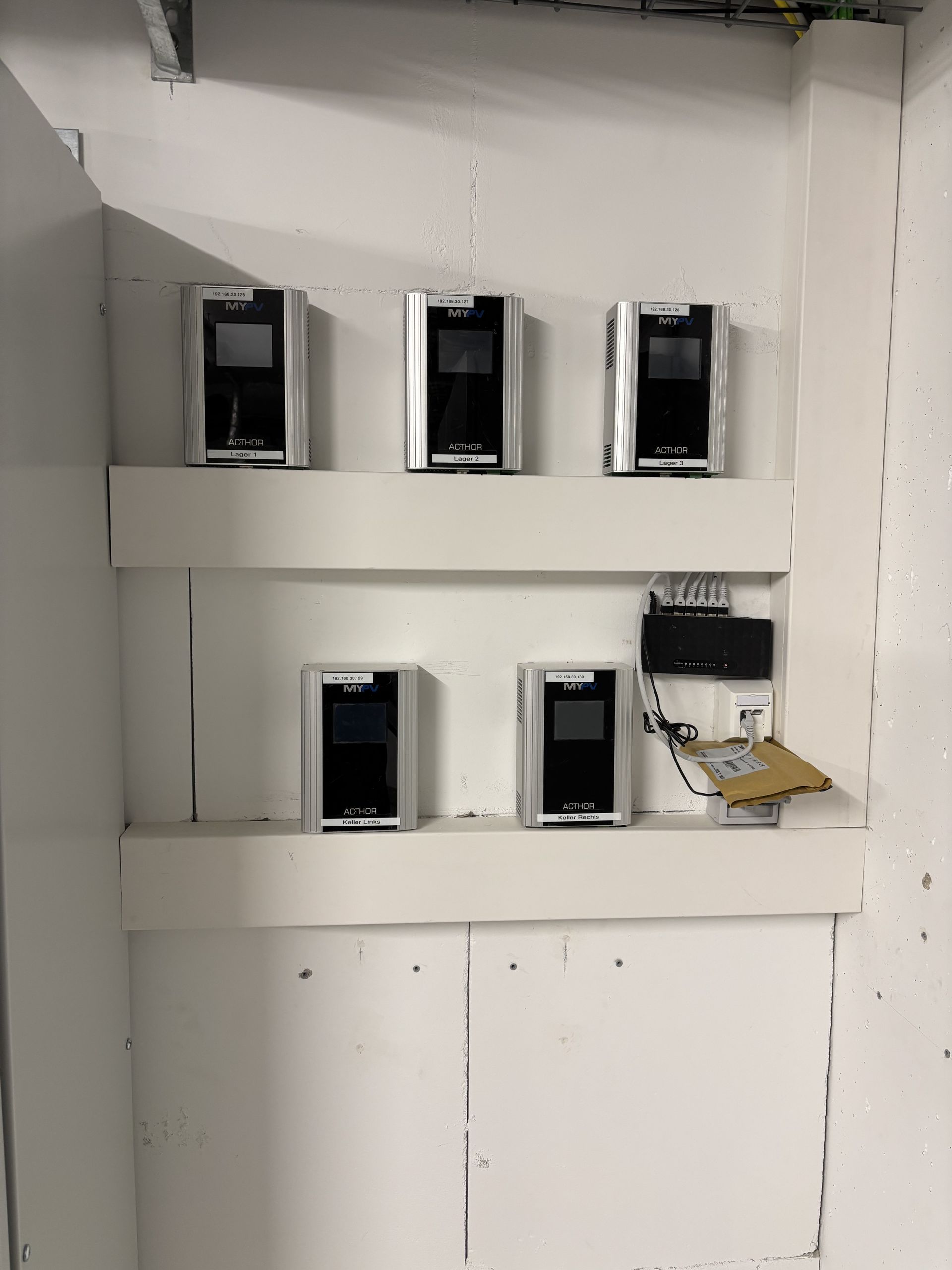 Five wall-mounted MYPV Acthor devices on white shelves, with connected network equipment and wiring on the right.
