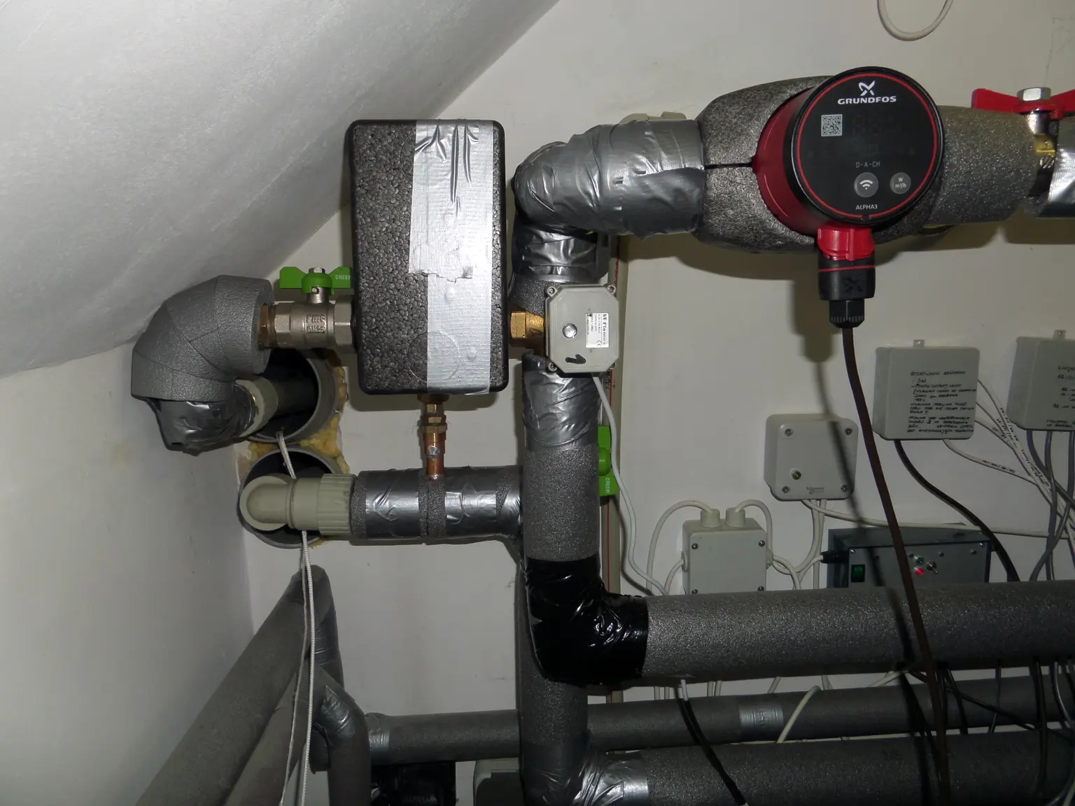 Pipes and valves in a utility room with insulation, tape, a pressure gauge, and connected electrical components.