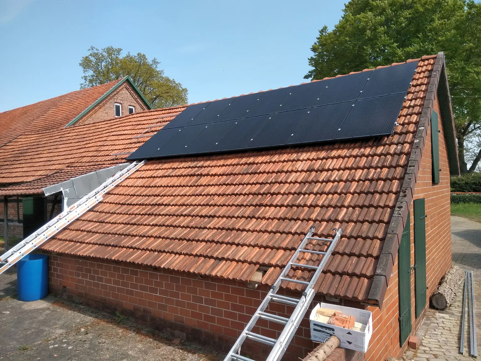 Tile-roofed shed with installed PV modules on the roof, with ladders and mounting materials in front.