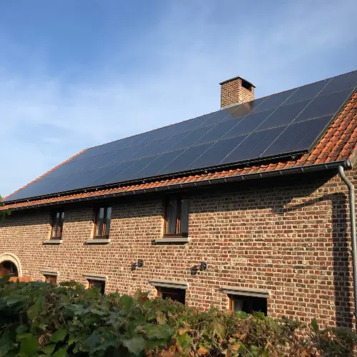 Brick house with red-tiled roof and solar panels, clear blue sky, greenery in the foreground