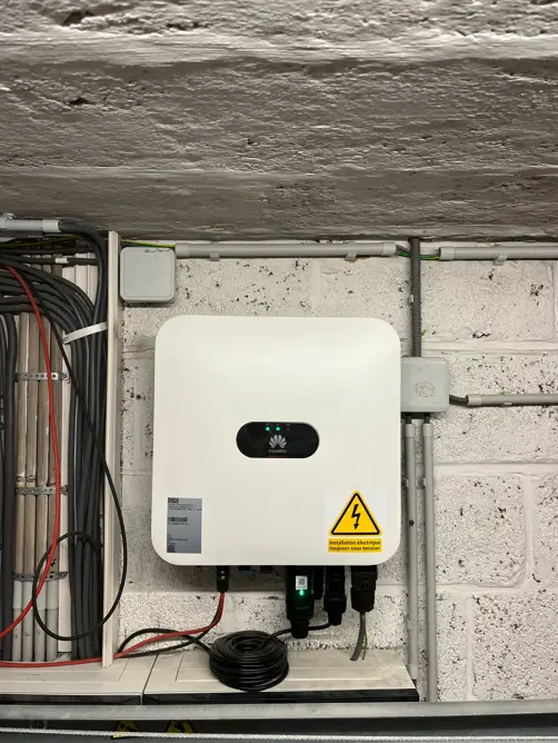 White electrical device mounted on a brick wall, surrounded by cables, with a caution sign indicating high voltage.