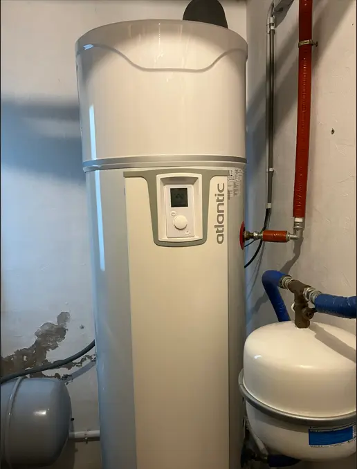 Tall white water heater with a digital display, labeled "Atlantic," connected to pipes in a utility room.