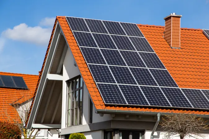 House with red-tiled roof featuring solar panels on top, clear blue sky in the background.