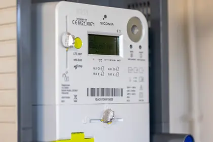 Close-up of a digital smart meter displaying readings and various labels, installed on a wall with visible connectors and indicators.