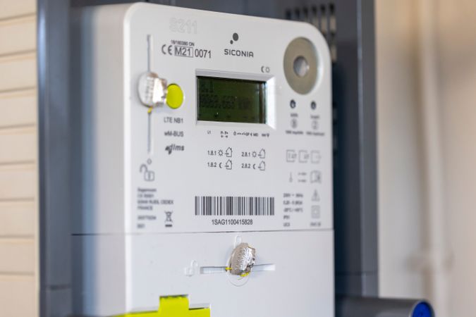 Close-up of a digital electricity meter with a small display screen, labeled buttons, and a visible barcode.