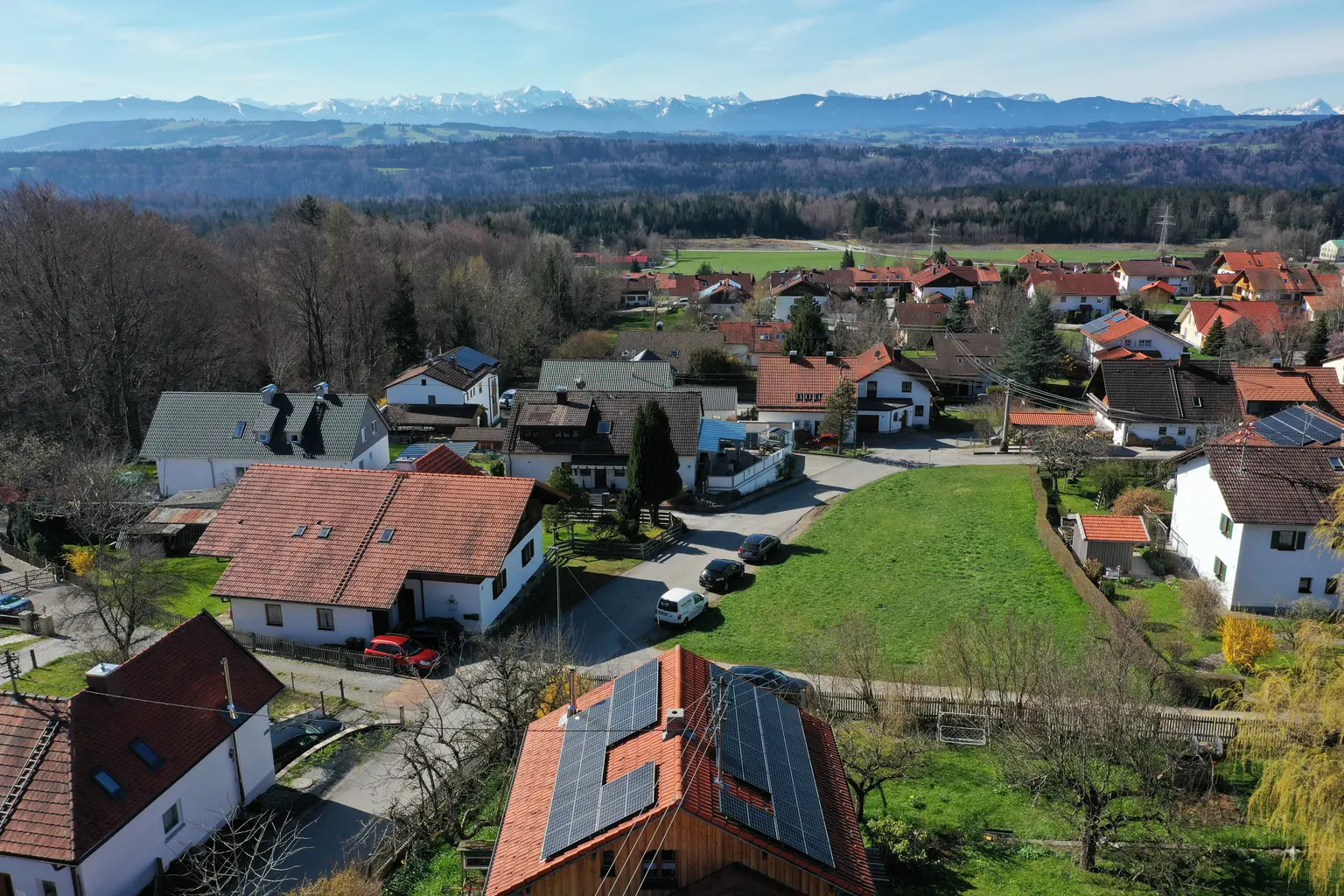 A residential area in Germany with PV panels on the roof of the front house. Behind the houses, a forest begins and mountains are visible.