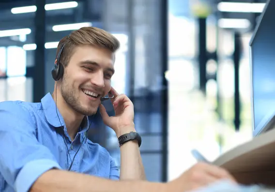 Smiling man in customer service is talking on the phone and simultaneously taking handwritten notes with a pen.