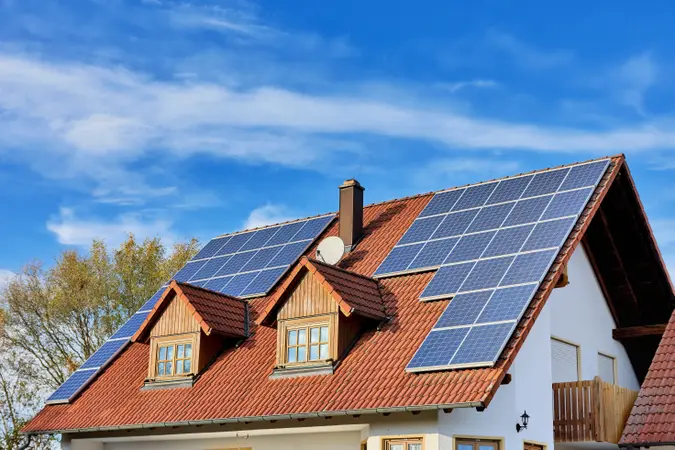 White house with red roof and solar panels, chimney, clouds in the sky, and a tree in the background.