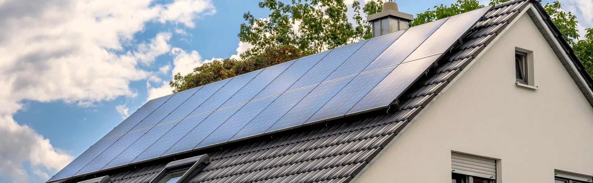 Single-family house with a PV system on the roof, with a leafy tree in the background.