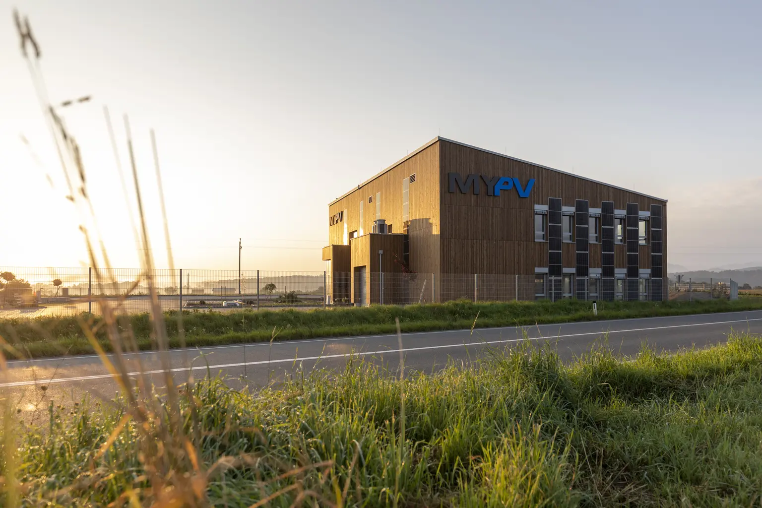 Company building at sunset with visible logo, blurred grass in the foreground, and atmospheric sky in the background.