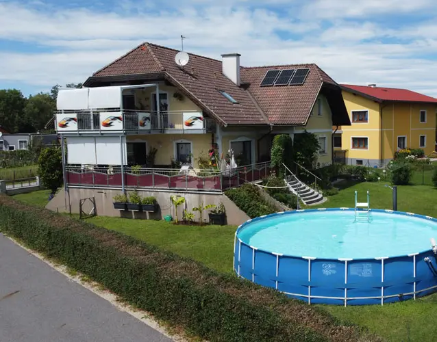 Two-story house with sloped roof, solar panels, and balcony, yard with round above-ground pool and well-kept lawn