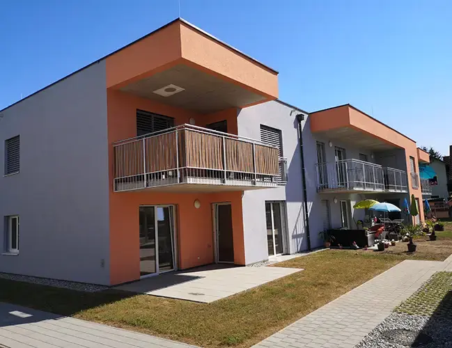 Modern two-story residential building with gray and orange facade, featuring terraces and balconies.