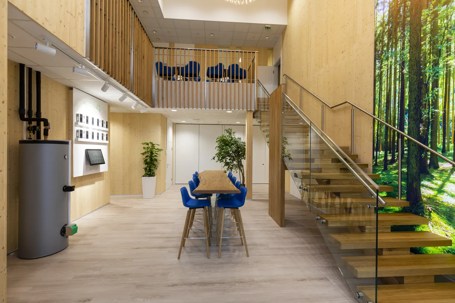 Foyer front view with standing table and chairs at entrance. On right, stairs lead up, beside them hangs a large forest picture.